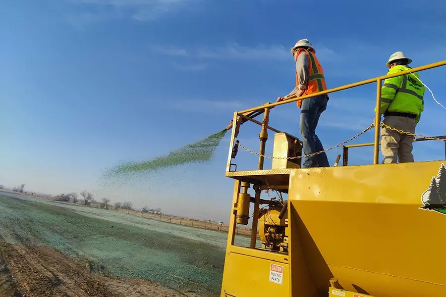 landscape technicians applying hydroseed from a hose while on a truck