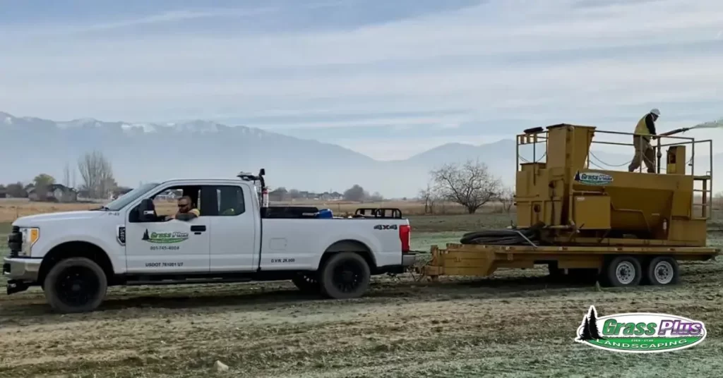 A pickup truck and a landscaping machine on a field.